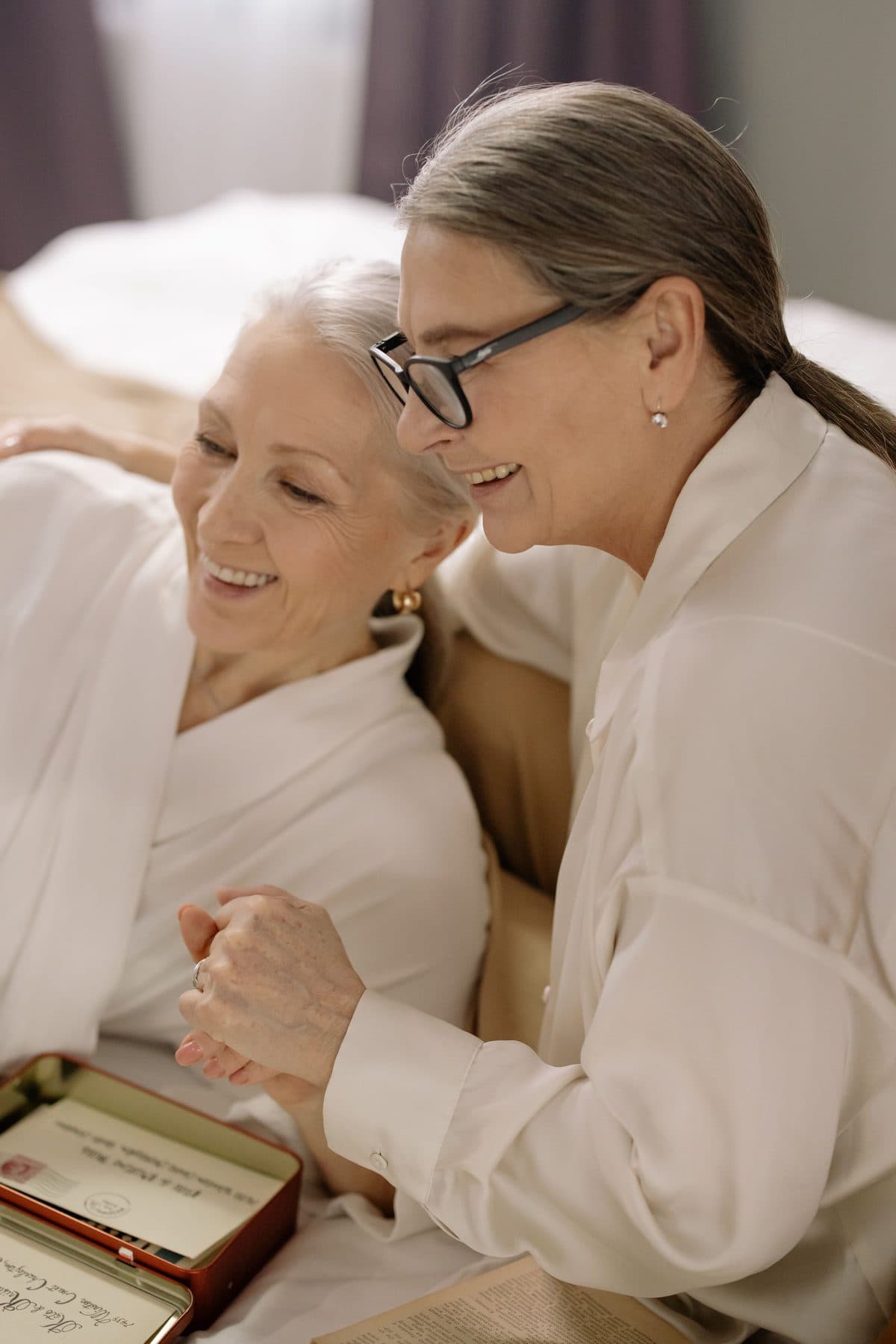 Two women side by side, smiling over a box of keepsakes and old letters.